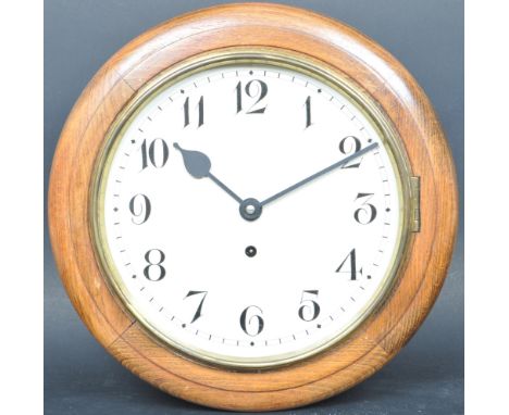 An early 20th century 24 hour wall hanging postmans / station clock having a circular oak frame with Arabic numerals to the c