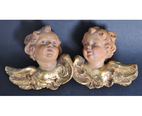 A pair of wooden early 20th century carved architectural cherub / putti heads. Each with gilded painted wings with painted we