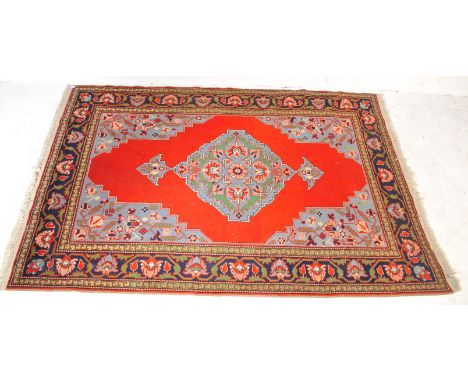 A large Kurdish old carpet floor rug with central blue medallion on red ground having decorative blue corner spadrels and geo