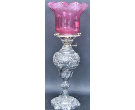 A Walker &amp; Hall silver plated oil lamp. The chase decorated plated body with a cranberry glass shade and clear glass flue