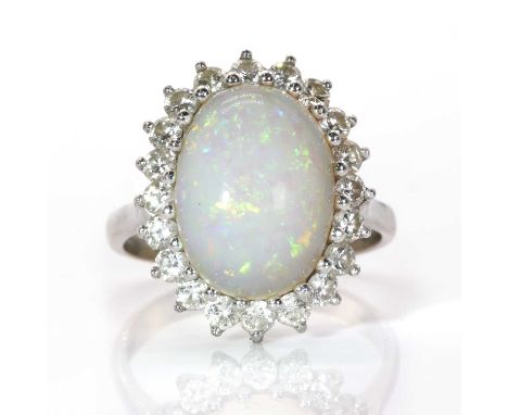 A white gold opal and diamond oval cluster ring, centring an oval cabochon opal within a surround of round brilliant cut diam