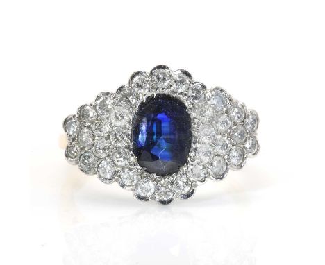 A sapphire and diamond plaque ring,  with an oval cut deep blue sapphire in a border extending over the shoulders of pavé set