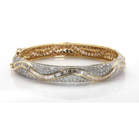 A vari-cut diamond hinged bangle,with a central row of tapered baguette cut diamonds, channel set to wave design guards, over