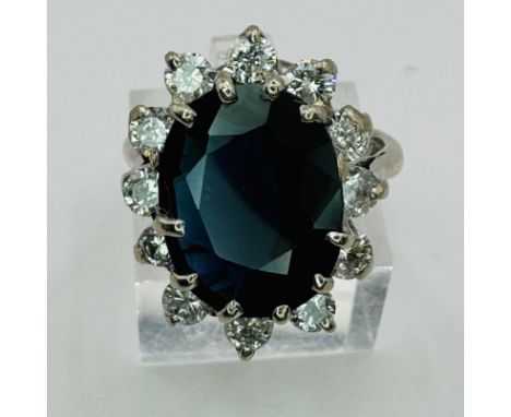 A large sapphire and diamond cluster ring in 18ct white gold. The dark blue, oval mixed cut sapphire, measuring approximately