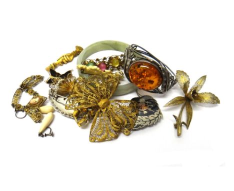 A treated amber oval hinged bangle, decorated with foliate motifs, a reconstituted jade bangle, a filigree butterfly brooch, 