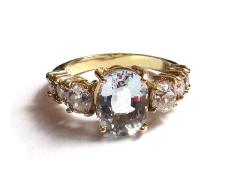 A diamond and pale blue gem set ring, claw set with the oval cut pale blue gem at the centre, between diamond set three stone