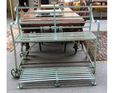 An early 20th century green painted wrought iron garden bench on a pair of end wheels, 123cm wide.