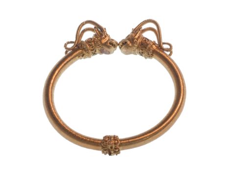 A Greek gold circular sprung hinged bangle, the terminals formed as classical stylised goat's head masks in the Hellenistic s