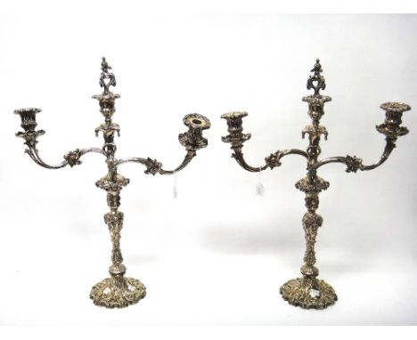 A pair of Victorian plated three light table candelabra, in a rococo revival design, each with scrolling arms with foliate mo