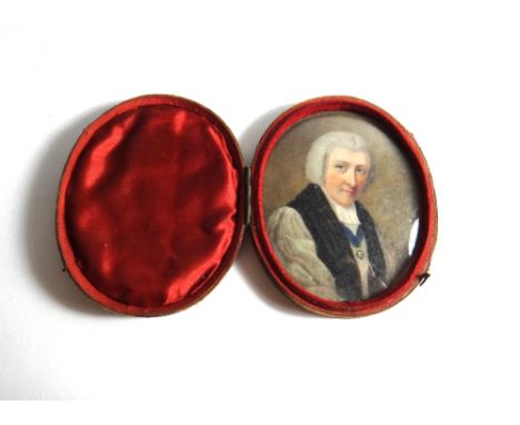 An oval portrait miniature of a clergyman, with grey hair wearing a white surplice and an enameled medal, displayed in an ova