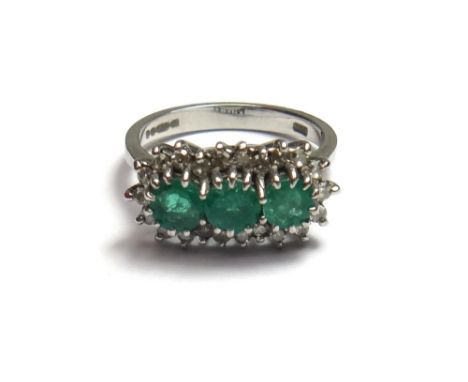 An 18ct white gold, emerald and diamond set ring, claw set with a row of circular cut emeralds at the centre within a surroun