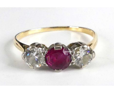 A yellow and white metal, ruby and diamond three-stone ring, featuring a centre round faceted ruby with a round brilliant cut