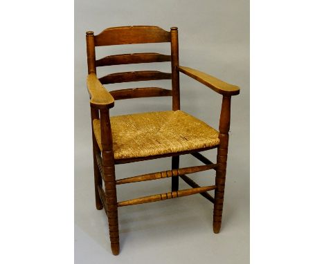 An oak rush seat ladder back elbow chair in the style of Gordon Russell the back with four concave rails, broad flattened arm