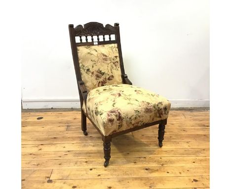 A late Victorian easy chair, the carved top rail incorporating a stylised foliate design, above an upholstered back and seat,