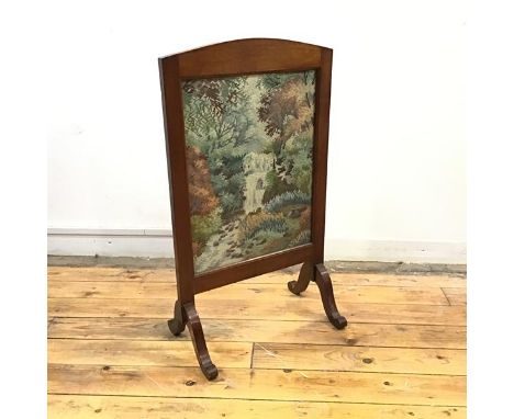 A 1940s mahogany framed firescreen, the arched top enclosing a grospoint tapestry banner depicting a waterfall in a wooded la