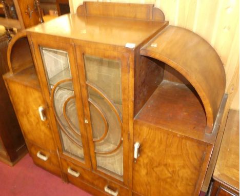 An Art Deco figured walnut ledgeback display cabinet, the twin central bevelled glazed doors within curved open compartments,