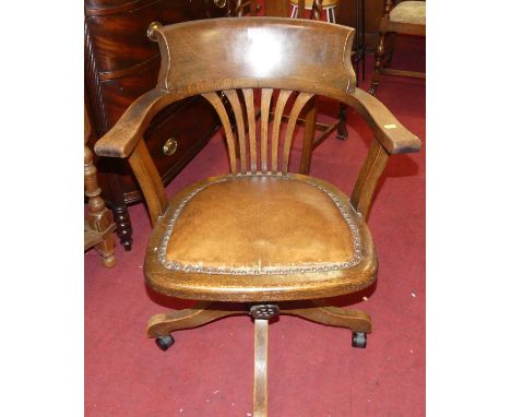 A 1930s oak tub splatback swivel desk chair, having a tan leather studded fixed pad seat and raised on later plastic roller c