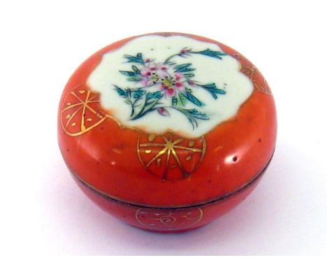 A Chinese porcelain covered pot in orange glaze, the top gilt and with an enamel floral spray. 7cm. diameter. 