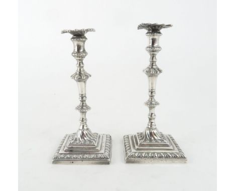 A NEAR PAIR OF GEORGE III CAST SILVER CANDLESTICKS on square footed and gadrooned bases, with swirl cast centre, knopped stem