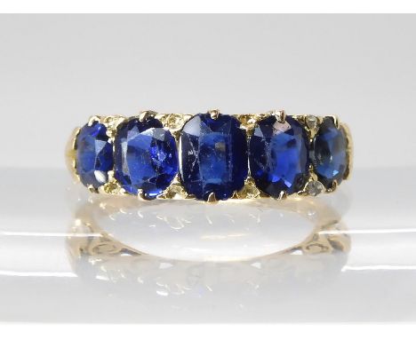 A FIVE SAPPHIRE RING in a classic yellow metal scrolled mount. Largest sapphire measures approx 5.99mm x 4.8mm x 2.68mm to sm