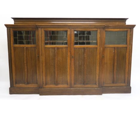 AN EARLY 20TH CENTURY OAK BREAKFRONT BOOKCASE with four leaded glass oak panel doors, 138cm high x 220cm wide x 41cm deep Con