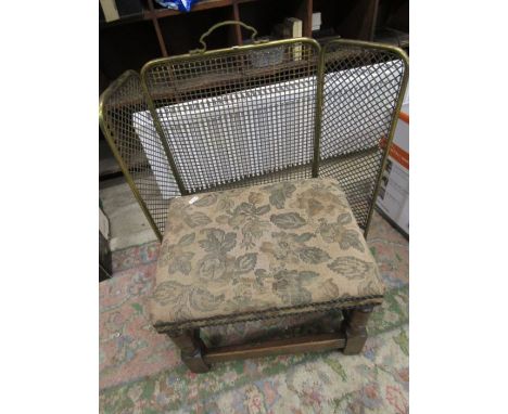 A brass fire guard and vintage stool with green tapestry cover
