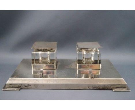 A rectangular silver inkstand, with two square glass inkwells, each with silver mounts, hinged covers with engine turned deco