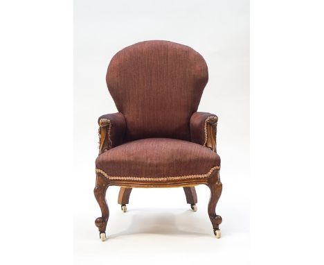 A Victorian mahogany nursing chair with foliate scroll arms, serpentine apron and cabriole legs on ceramic casters