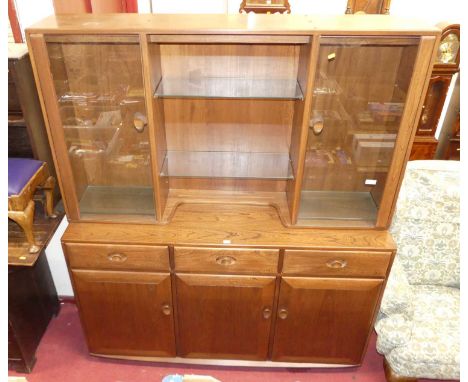 A contemporary Ercol mid-elm wall unit, having twin upper glazed doors and open shelving, over base with three frieze drawers