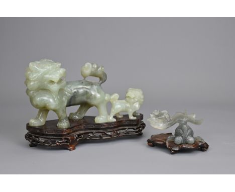 TWO CHINESE CARVED JADE SERPENTINE FIGURES ON WOODEN STANDS, 20TH CENTURY. A carving of lion dog and pup on a carved and pier