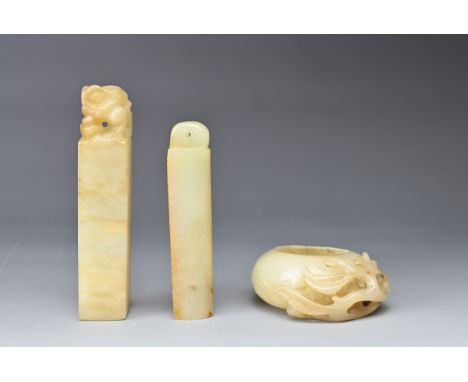 A CHINESE CARVED JADE BRUSH WASHER AND TWO SEALS. All pale in hue, the peach-shaped brush washer with carved pierced leafy br