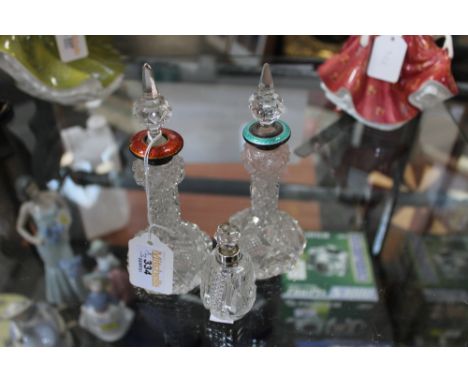 Two cut glass perfume bottles with silver enamelled tops and one with silver collar