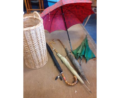 A collection of parasols and walking sticks housed in a wicker umbrella/stick stand to include five vintage parasols and umbr