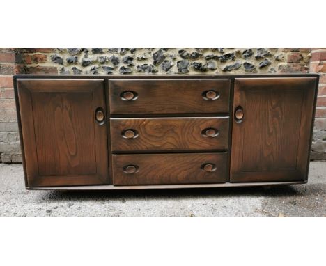 A dark elm Ercol sideboard, with three central drawers, one with cutlery drawer, flanked either side with a cupboard enclosin