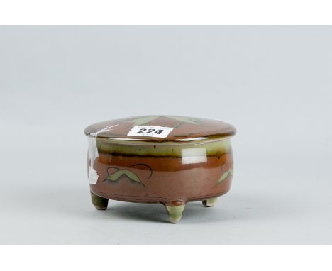 A David Frith circular trinket pot and cover on three feet, green celadon type and brown background with stylized patterns to