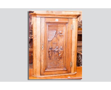 A small reproduction carved oak corner cupboard, the single opening door with inset carved panel depicting people before a co