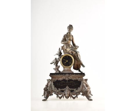 A 19th century French spelter mantel clock. The figure of a lady feeding sparrows is perched above the dial, mounted on a pol