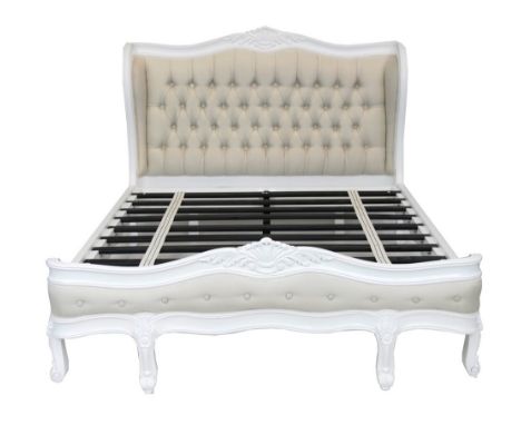 A French style white upholstered king size bedWith a leafy crest above a button back upholstered head board raised on scroll 