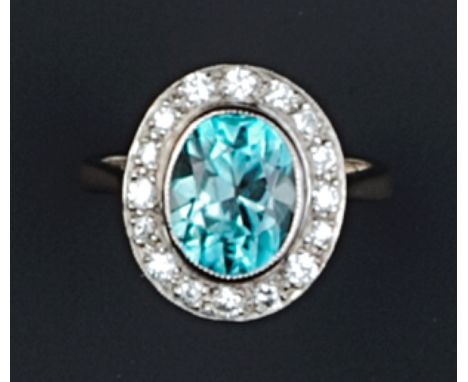A ZIRCON AND DIAMOND CLUSTER RING, the oval mixed-cut blue zircon framed by a brilliant-cut diamond border, in millegrain col
