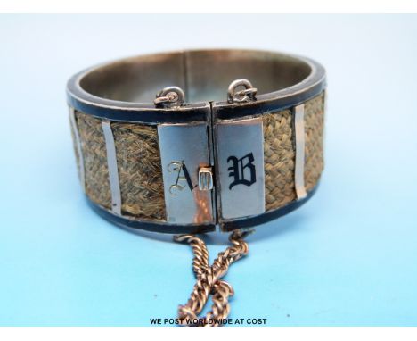 A Victorian white metal bangle decorated with plaited hair and black enamel with initials A.B and dated 1882