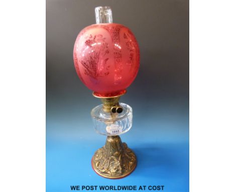 A late 19th/20thC oil lamp with acid etched globe-shaped shade, cut glass reservoir raised on circular base with three goat m