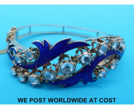 A yellow metal bangle set with 13 rose cut diamonds and blue enamel in a scrolling foliate design