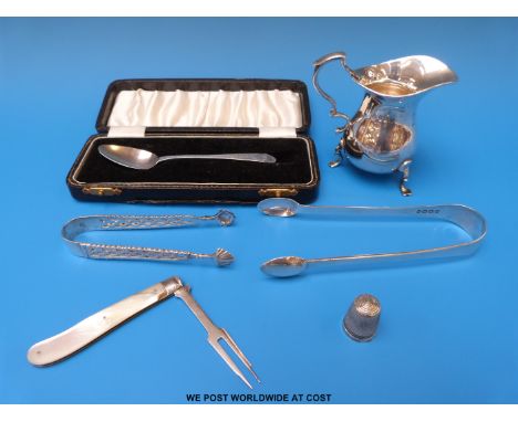 A hallmarked silver cream jug, Georgian sugar tongs, another pair of hallmarked silver sugar tongs, silver thimble and a case