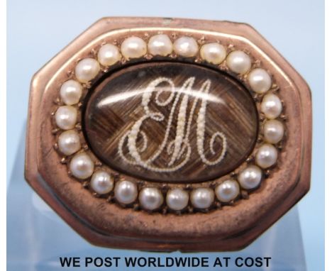 A Georgian yellow metal brooch set with a central panel of plaited hair with initials made up of seed pearls surrounded by a 