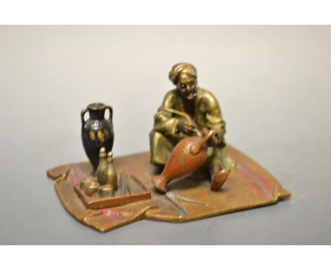 A Vienna style painted bronze Arab street vendor painting a pottery vase, seated upon a carpet