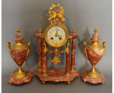 A French Rouge Marble and Gilt Metal Mounted Three Piece Clock Garniture, the central portico clock with enamel dial and two 