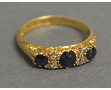 An 18ct Yellow Gold Sapphire and Diamond Band Ring, set with three sapphires and four diamonds within a pierced setting