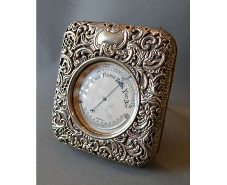 A Late 19th Century Large Table Barometer Thermometer within a silver case decorated in relief with scrolls within foliage, 1