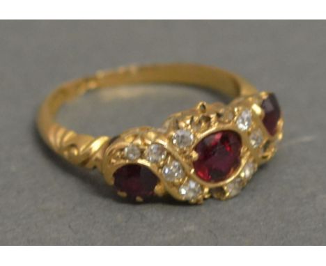 An 18ct Yellow Gold Ruby and Diamond Ring set with three rubies surrounded by diamonds within a pierced setting