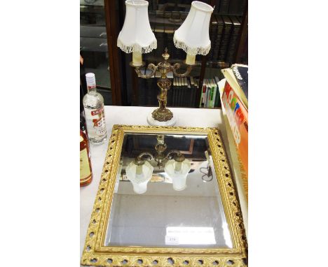 A gilt framed wall mirror; a two branch figuratively table lamp. 
